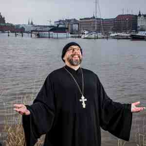 ortodoksipappi isä Johannes Lahtela seisoo meren rannalla Helsingissä kädet levitettyinä ja katse kohti taivasta
